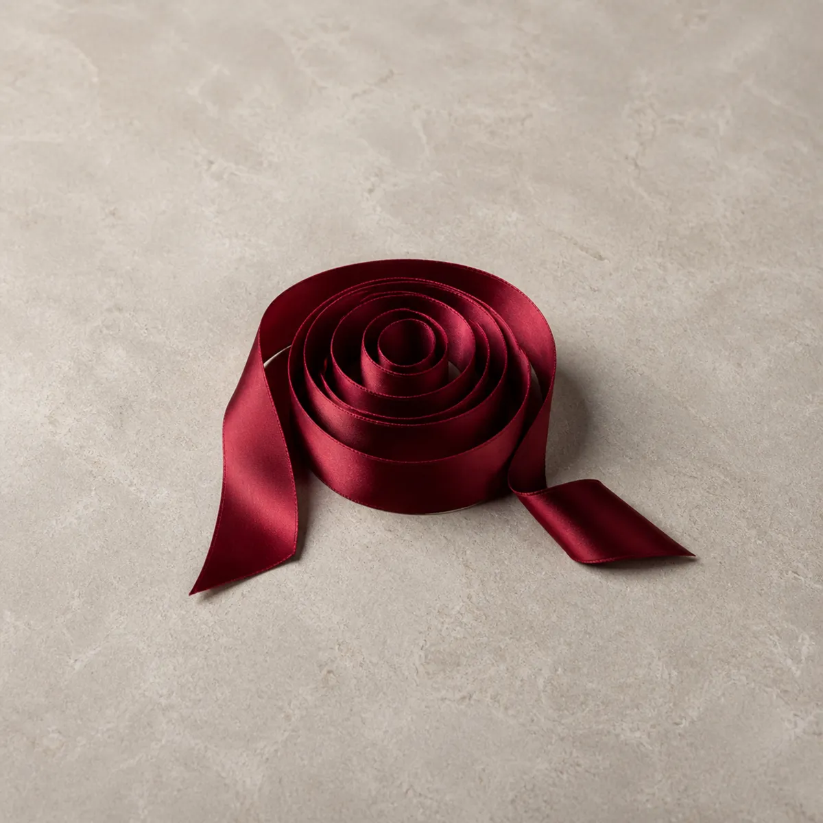 A coil of deep red silk ribbon on pale stone